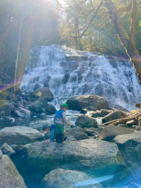 Two kids climbing on rocks at the base of Reed Brook Falls, a scenic cascade and swimming spot near Carrabassett Valley, Maine