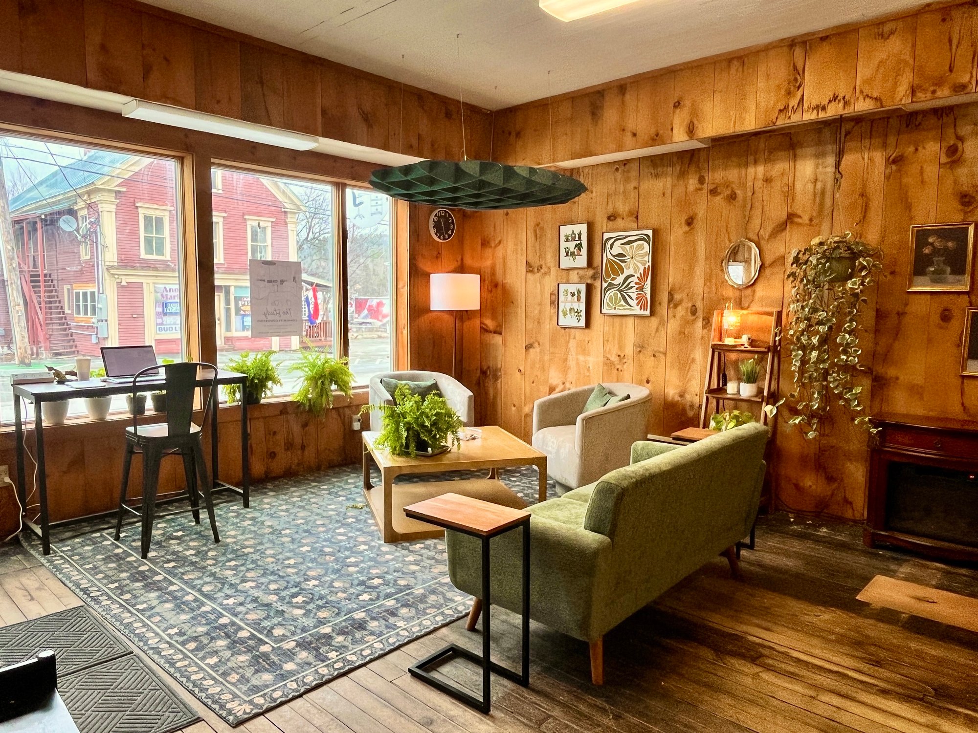 Lounge and window-facing workstation at The Study coworking space — comfortable seating, a standing desk with laptop, and natural light from Main Street windows.