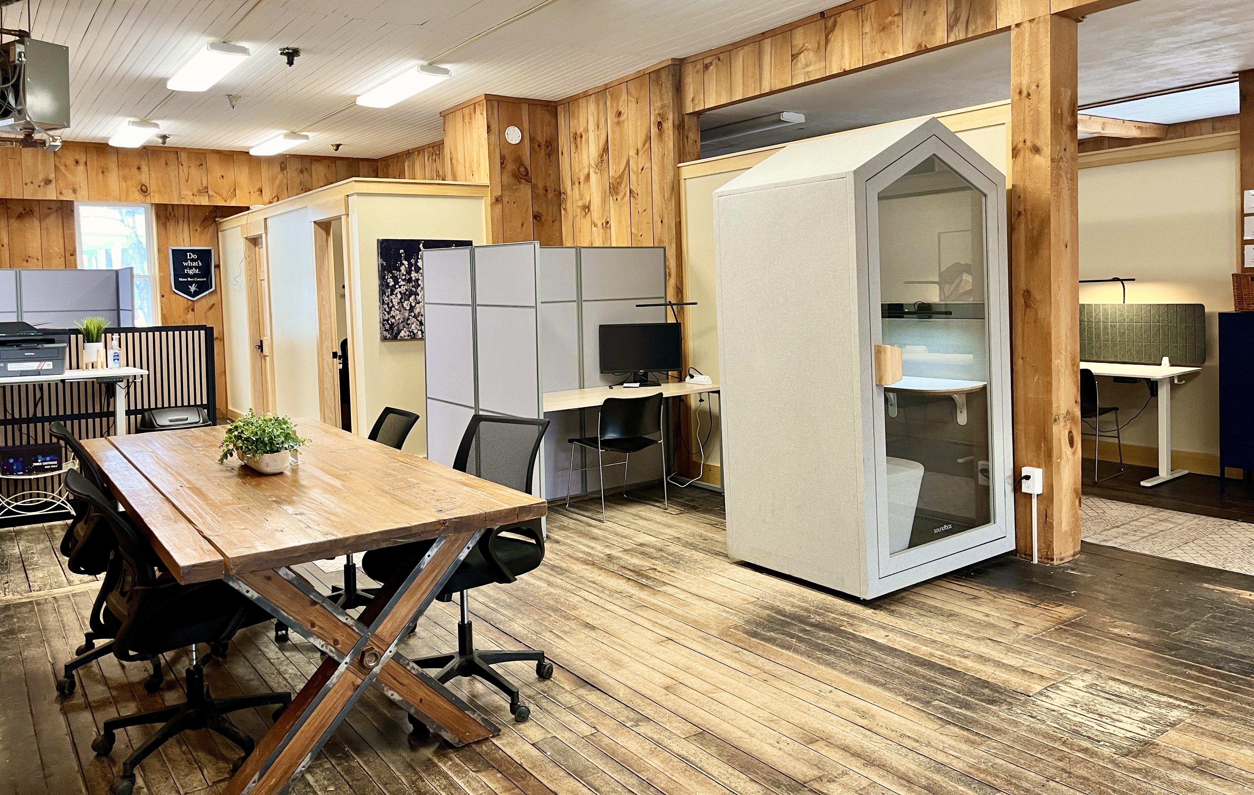 Interior of The Study coworking space in Kingfield, Maine, with a large communal work table, dedicated desks, and a private phone booth for video calls