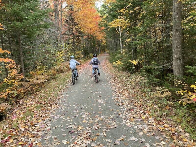 Two kids biking the Narrow Gauge Pathway, a flat multi-use trail along the Carrabassett River in Carrabassett Valley, Maine