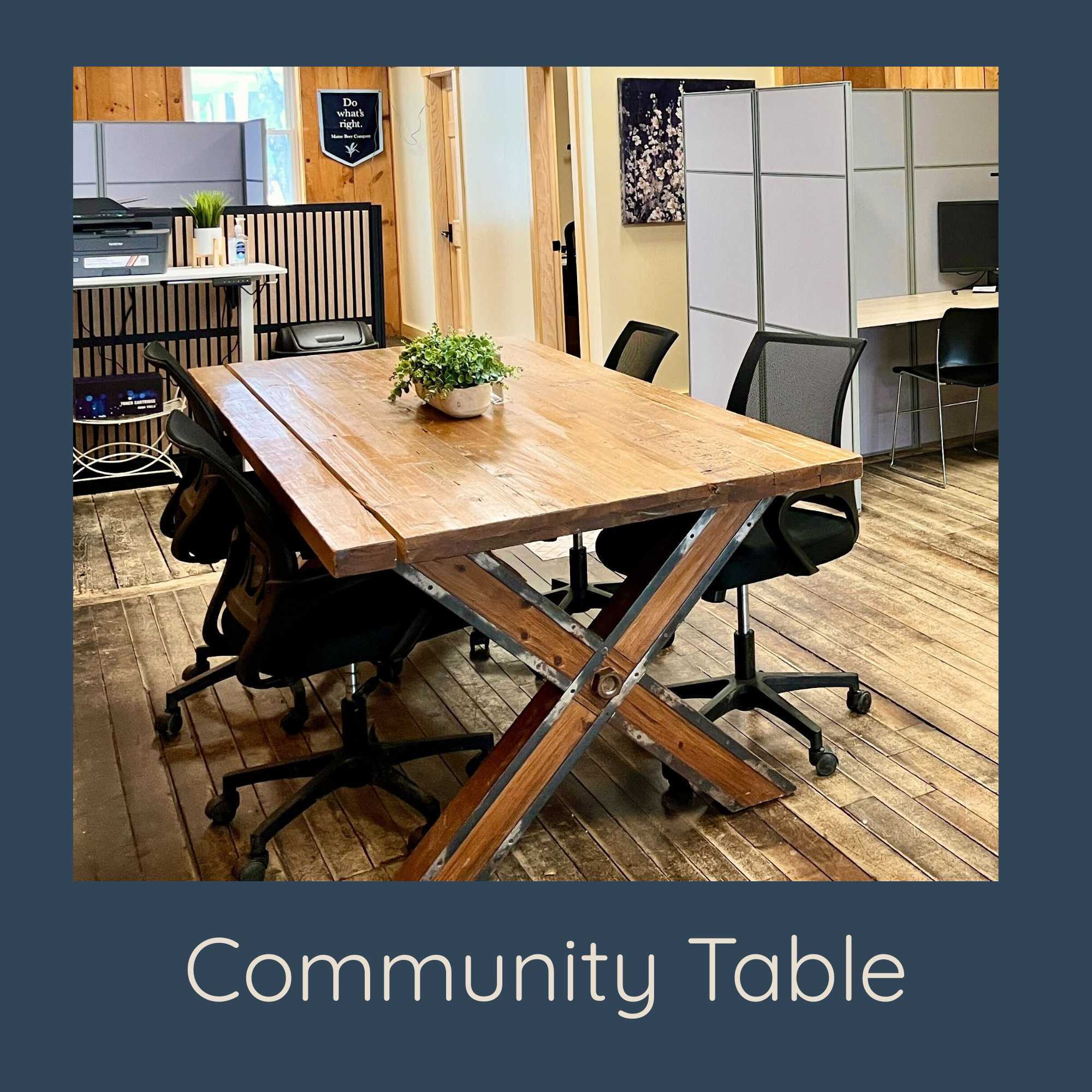 Community Table: "Large shared wooden community table surrounded by office chairs in a bright coworking room"